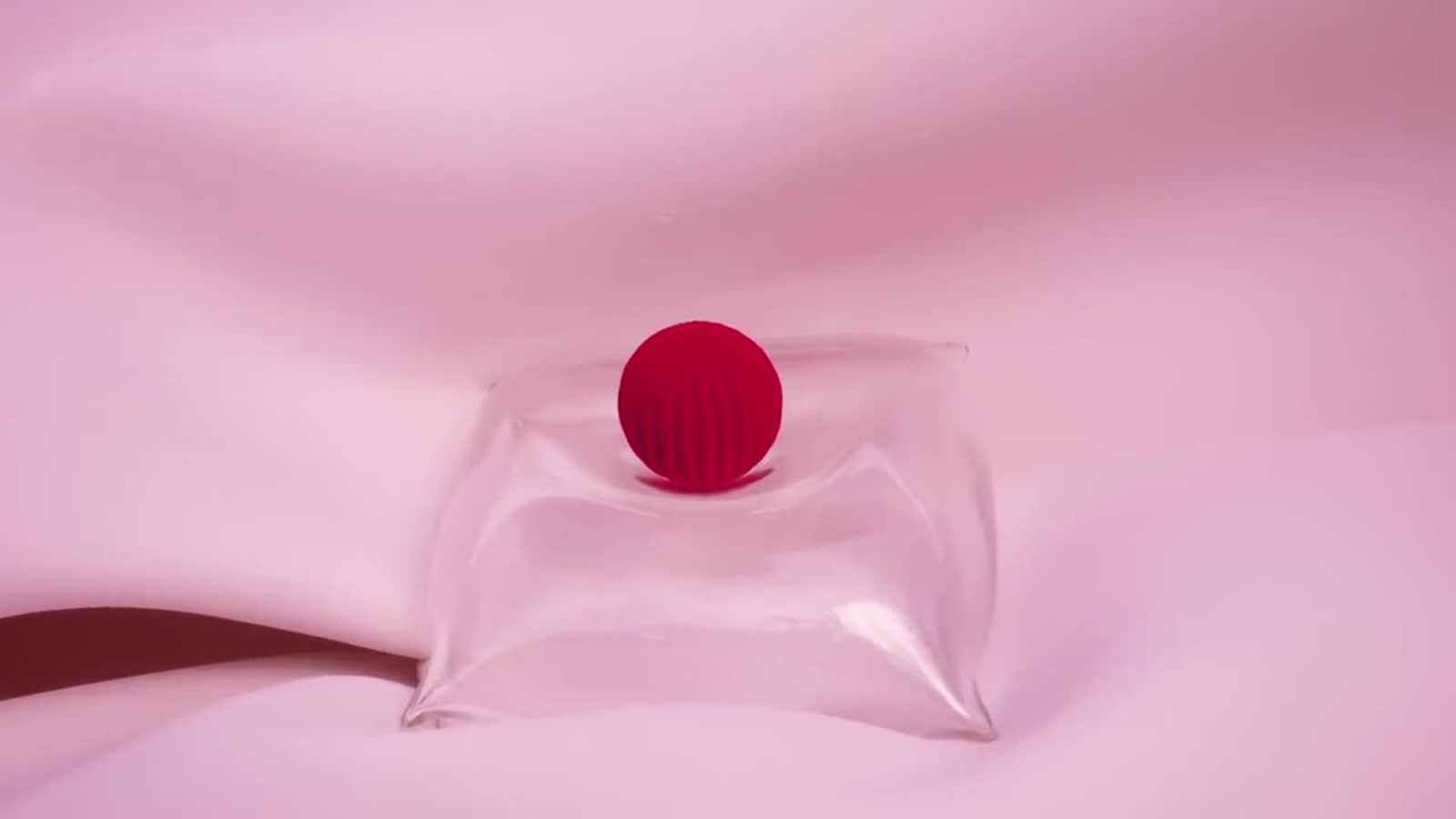 A red fluted sphere resting in a clear pouch on pink fabric, a frame from the film
